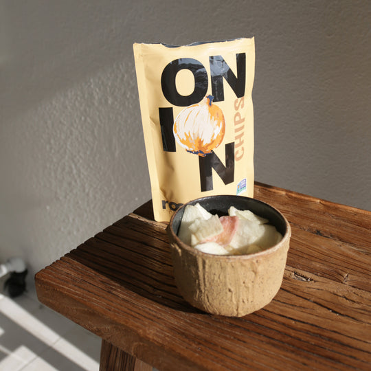 lifestyle image of Root Foods Onion Chips bag on a wooden table with roots onion veggie chips in a bowl